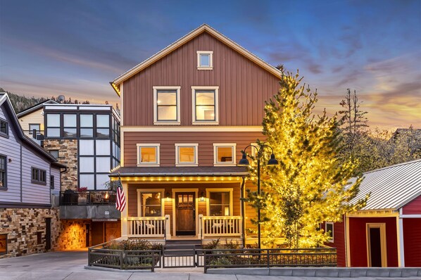 A two-story building with a porch, a flag, and a tree with lights. - The Peak At Town Lift 3 Bedroom Home (Park City)