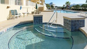 A swimming pool with a tiled edge, a sunshade, lounge chairs, and a lifeguard stand. - Indies 401 | 3BR/3BA Corner Condo | Sleeps 6 | Wraparound Balcony & Views (Gulf Shores)