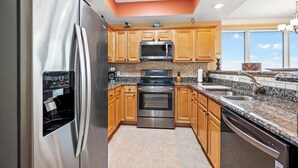 A modern kitchen with stainless steel appliances, wooden cabinets, granite countertops, and a large window providing natural light. - Indies 401 | 3BR/3BA Corner Condo | Sleeps 6 | Wraparound Balcony & Views (Gulf Shores)