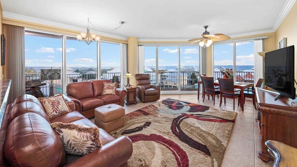 A spacious living room with a large window, leather sofa, and a dining area. - Indies 401 | 3BR/3BA Corner Condo | Sleeps 6 | Wraparound Balcony & Views (Gulf Shores)