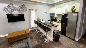 Una cocina moderna con barra, televisor montado en la pared y refrigerador.