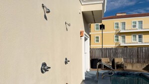 Une zone avec une piscine, entourée d’une clôture en bois, avec une chaise et un bâtiment doté de balcons en arrière-plan.