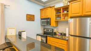 Une cuisine de taille réduite, dotée de meubles en bois, d’un réfrigérateur en acier inoxydable, d’un four à micro-ondes et d’une cuisinière.