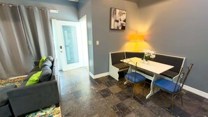 A modern living room with a grey sofa, a dining table with blue chairs, and a small table with a lamp and flowers. - Priced Right Near Beach Well Equipped 2 Bedroom Apts (South Padre Island)