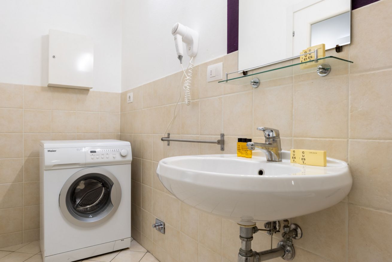 A modern bathroom with a white washing machine, a sink, and a mirror.