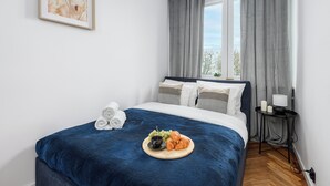 A neatly made bed with a blue blanket, a tray with croissants and grapes, and a framed picture on the wall. - Lumina 2-room apart near the Old Town (Warsaw)