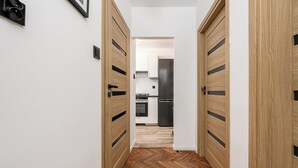 A hallway with wooden doors leading to a modern kitchen with black appliances. - Lumina 2-room apart near the Old Town (Warsaw)