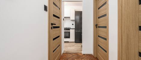 A hallway with wooden doors leading to a modern kitchen with black appliances.