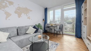 A modern living room with a sectional sofa, a glass coffee table, a world map on the wall, a dining area with a table and chairs, and a large window with curtains. - Lumina 2-room apart near the Old Town (Warsaw)