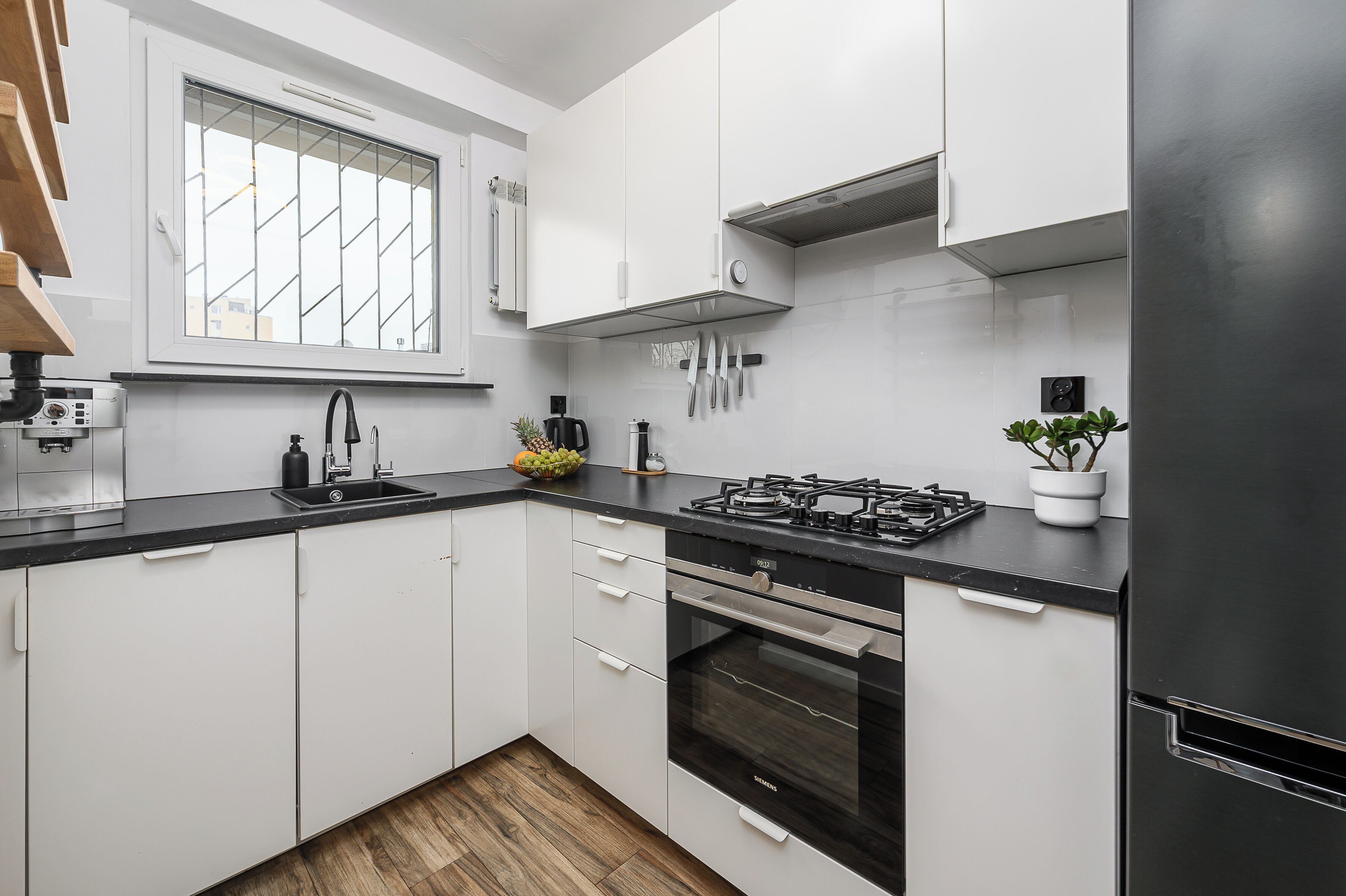 Una cocina moderna con armarios blancos, encimera negra, estufa a gas y refrigerador de acero inoxidable.