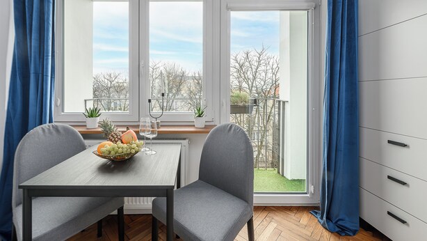 A dining area with a table, two chairs, a bowl of fruit, and a view of a garden through a large window. - Lumina 2-room apart near the Old Town (Warsaw)