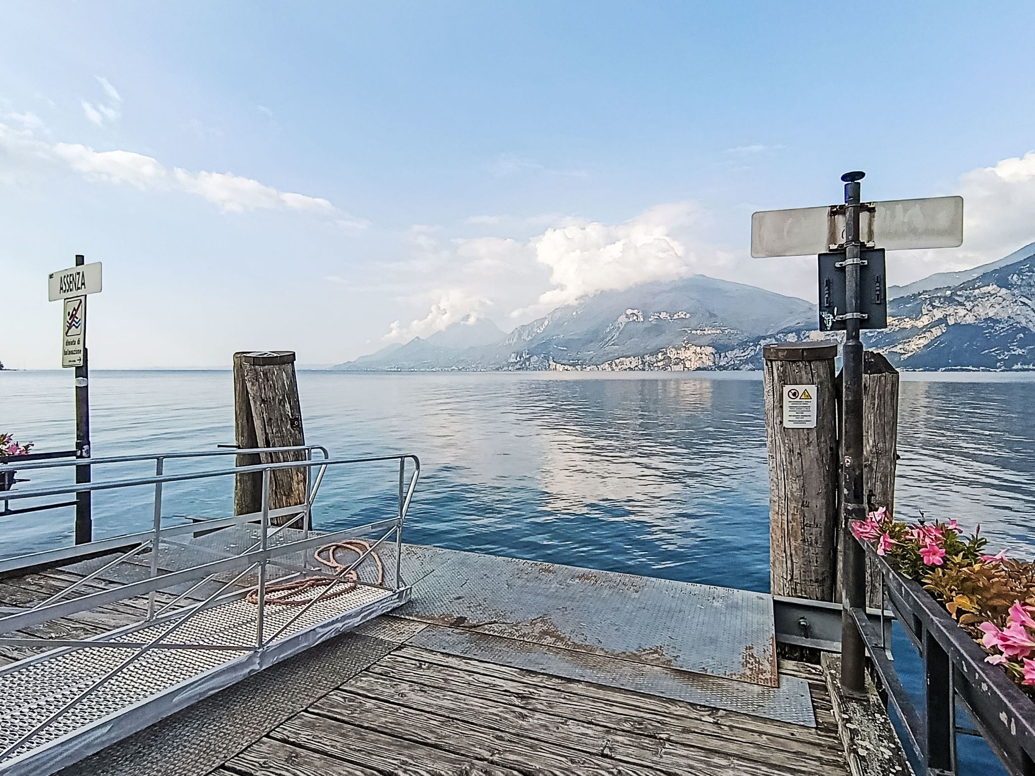 A pier with a metal railing, wooden posts, and a sign with a warning symbol.