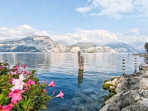 Ein ruhiger See mit Bergen im Hintergrund, ein Holzpfahl im Wasser und Felsen am Ufer.