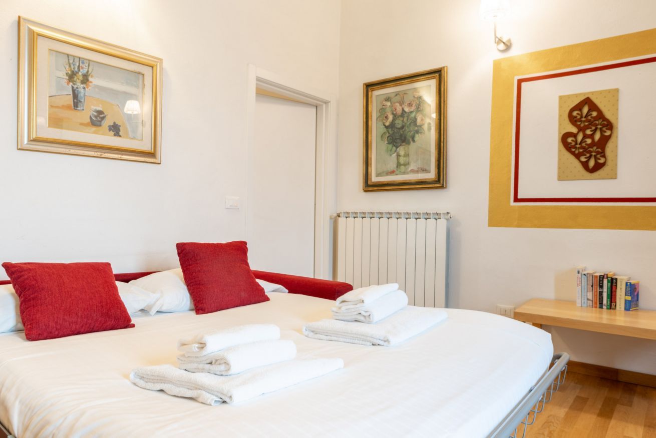 Une chambre d’hôtel avec un grand lit, des oreillers rouges et blancs, des serviettes soigneusement pliées et une bibliothèque remplie de livres.