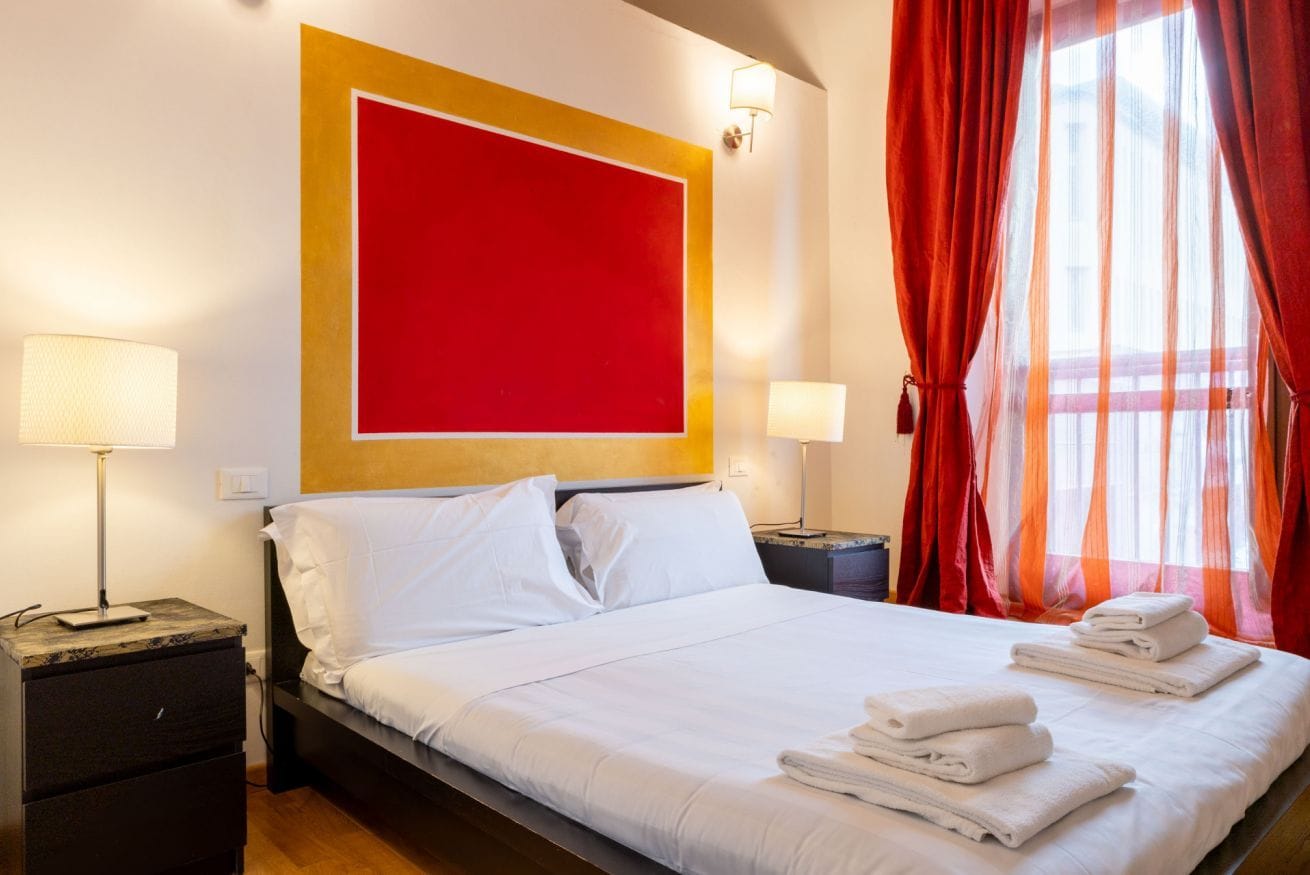Une chambre d’hôtel avec un grand lit, deux tables de chevet et un mur d’accent de couleur rouge.
