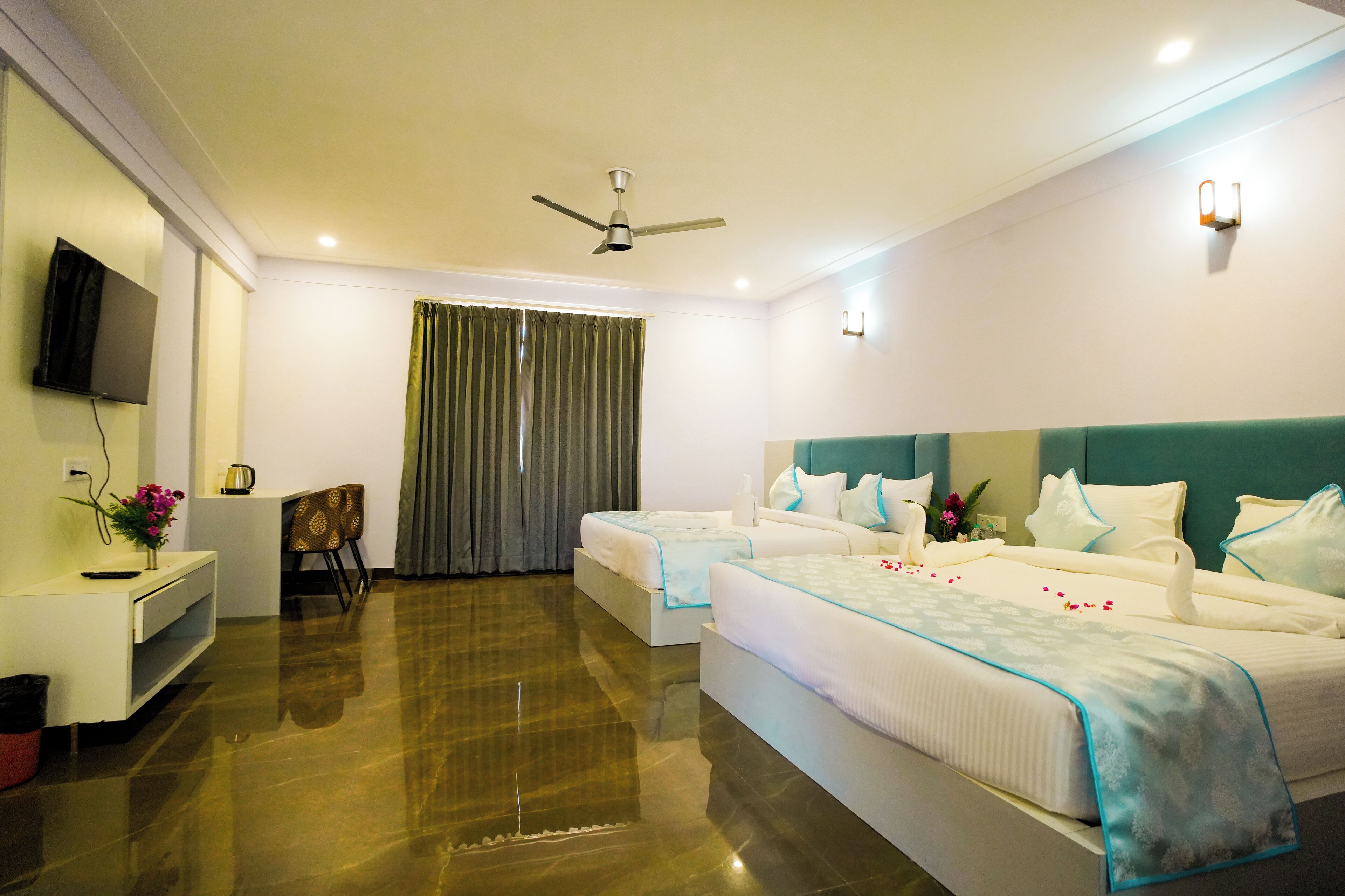 A hotel room with two beds, a TV, a desk, and a ceiling fan.