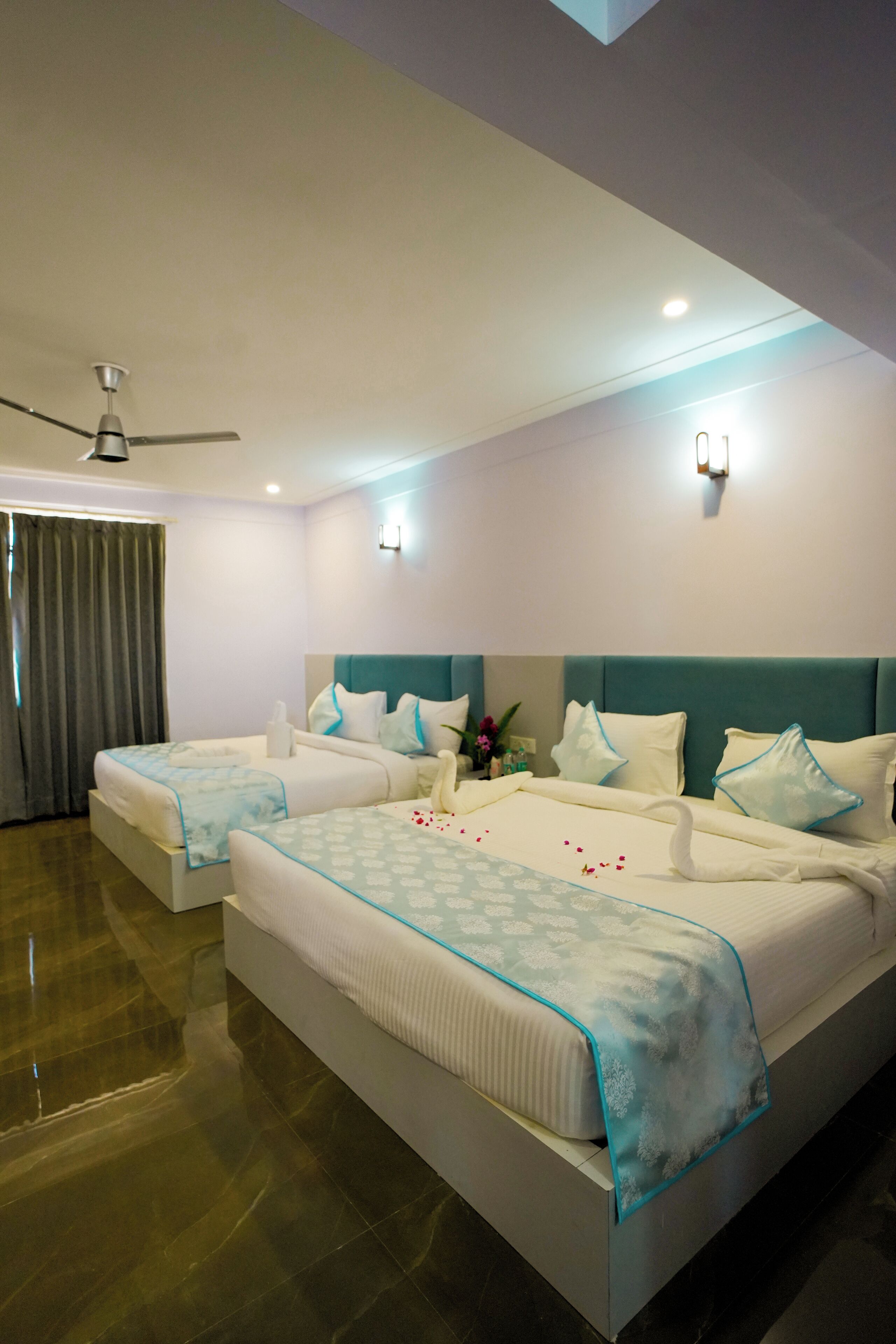 A hotel room with two beds, a ceiling fan, and a large window with curtains.