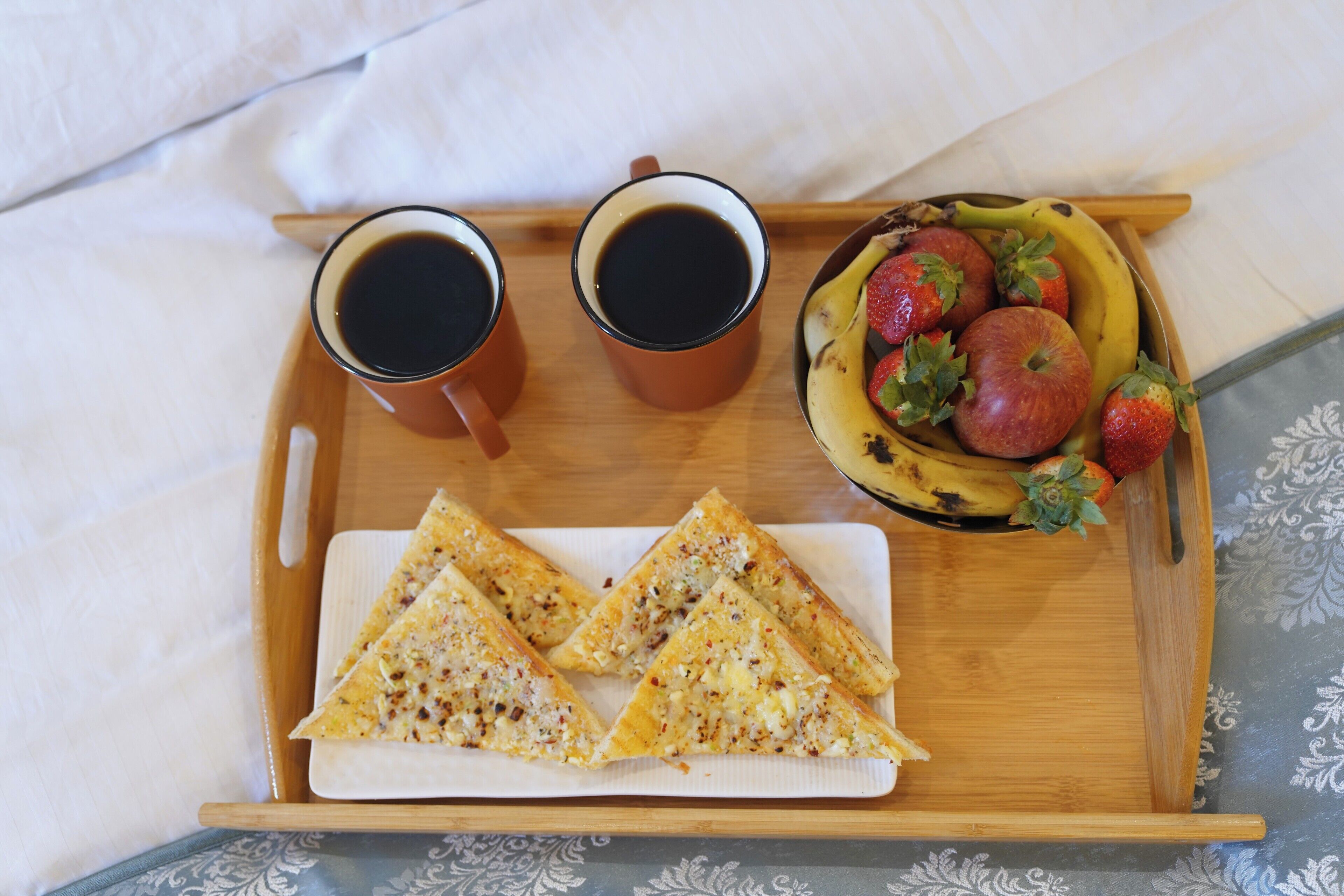Una bandeja con dos tazas de café, una banana, fresas y porciones triangulares de comida.
