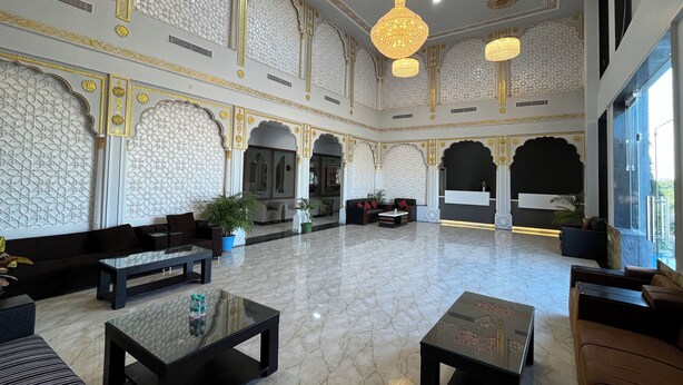 Een ruime lobby met gedetailleerde witte en gouden wanddecoraties, diverse zithoeken en moderne verlichtingsarmaturen.