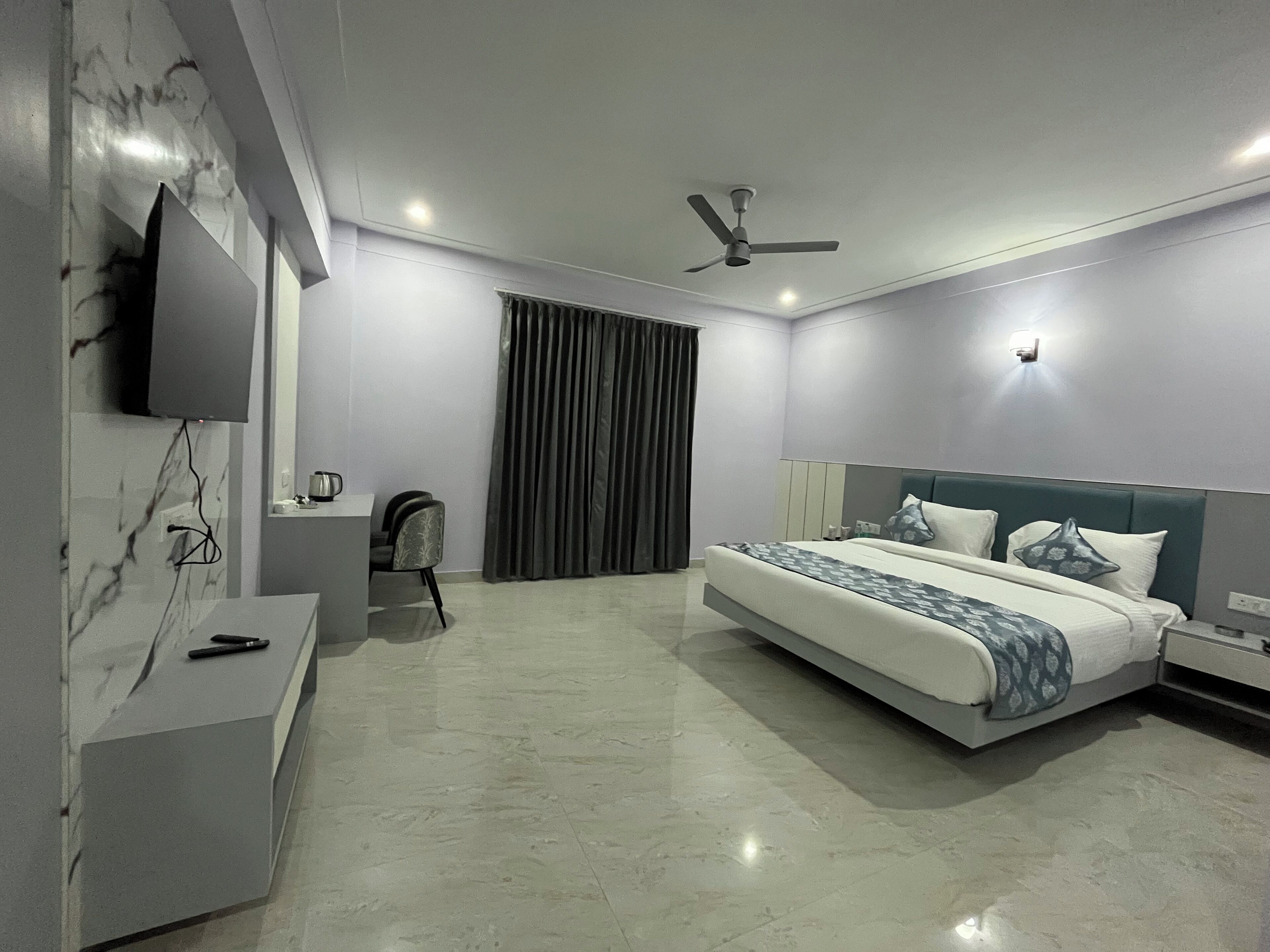 Een moderne hotelkamer met een groot bed, een flatscreen televisie aan de muur, een plafondventilator en een klein bureau met een stoel.