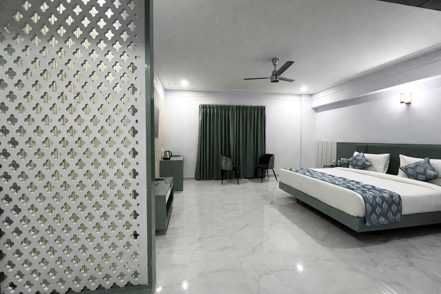 A modern bedroom with a bed, a desk, a chair, a ceiling fan, and a green curtain.