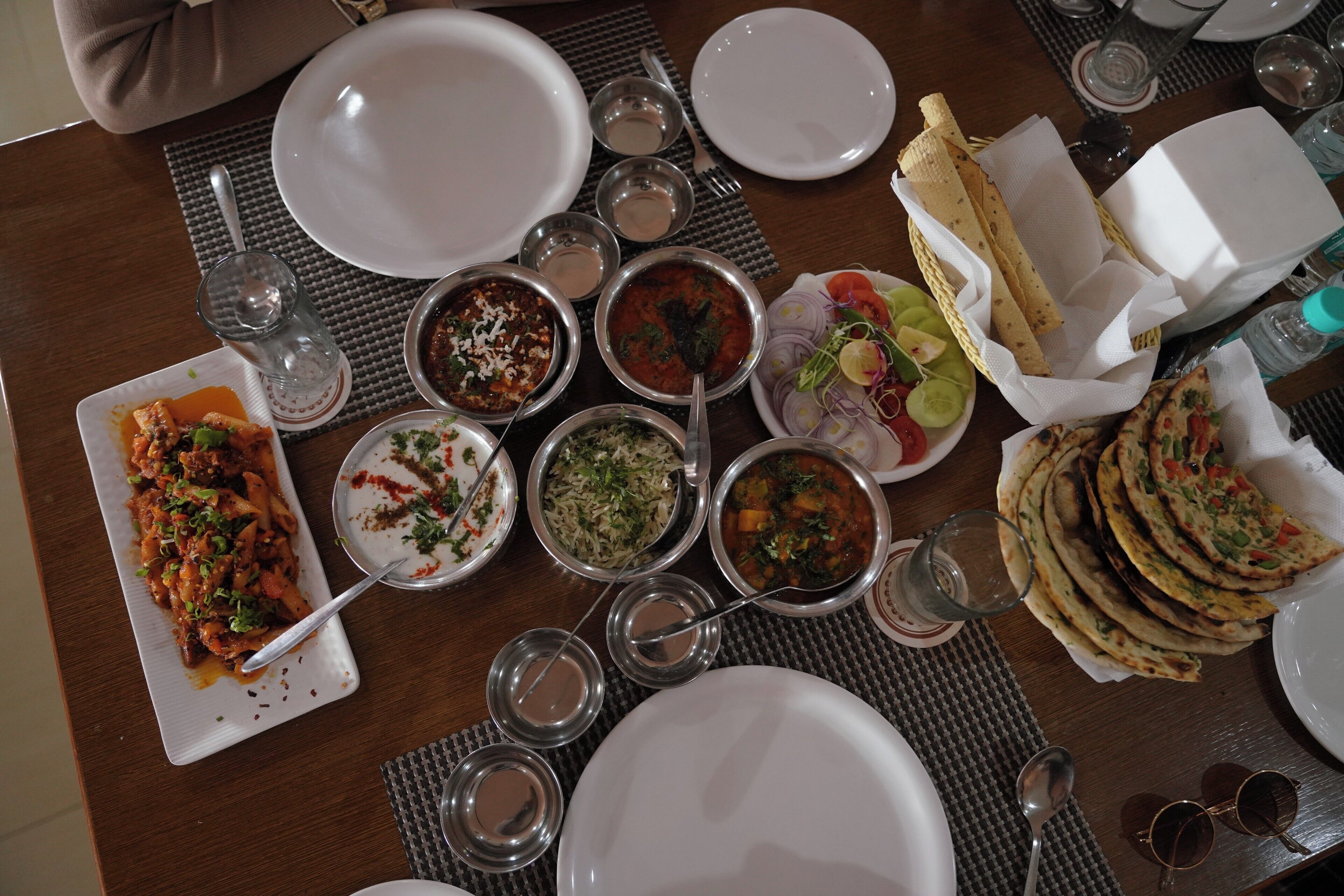 A table set with various dishes, including pasta, rice, and flatbreads, along with multiple glasses and cutlery.
