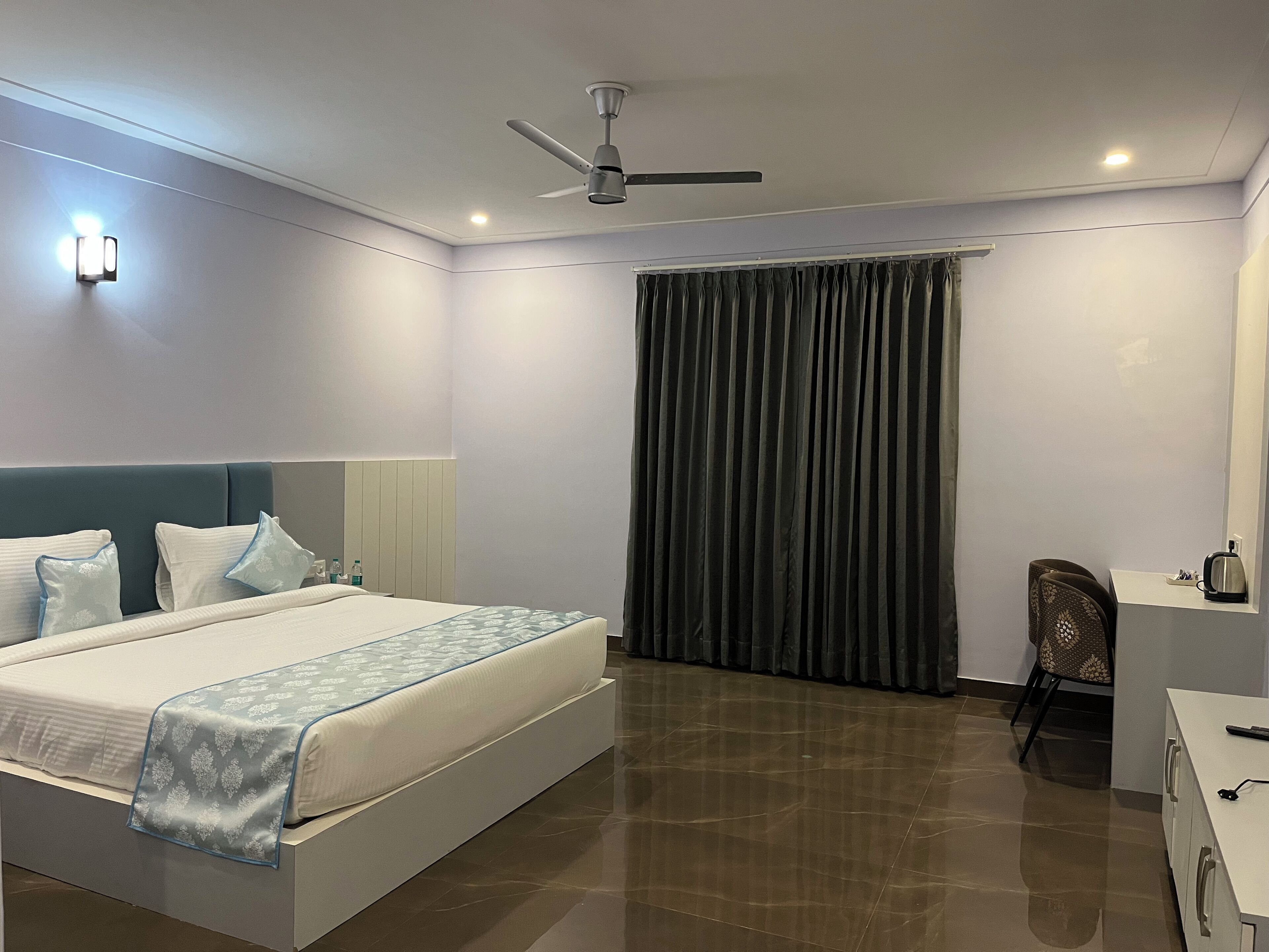 Une chambre d’hôtel équipée d’un lit, d’un bureau, d’une chaise, d’un ventilateur de plafond et d’une fenêtre avec des rideaux.