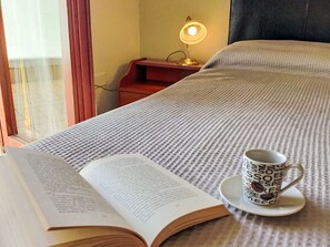 Ein Bett mit einer geblümten Decke, ein offenes Buch und eine Tasse mit Kaffeemotiv.