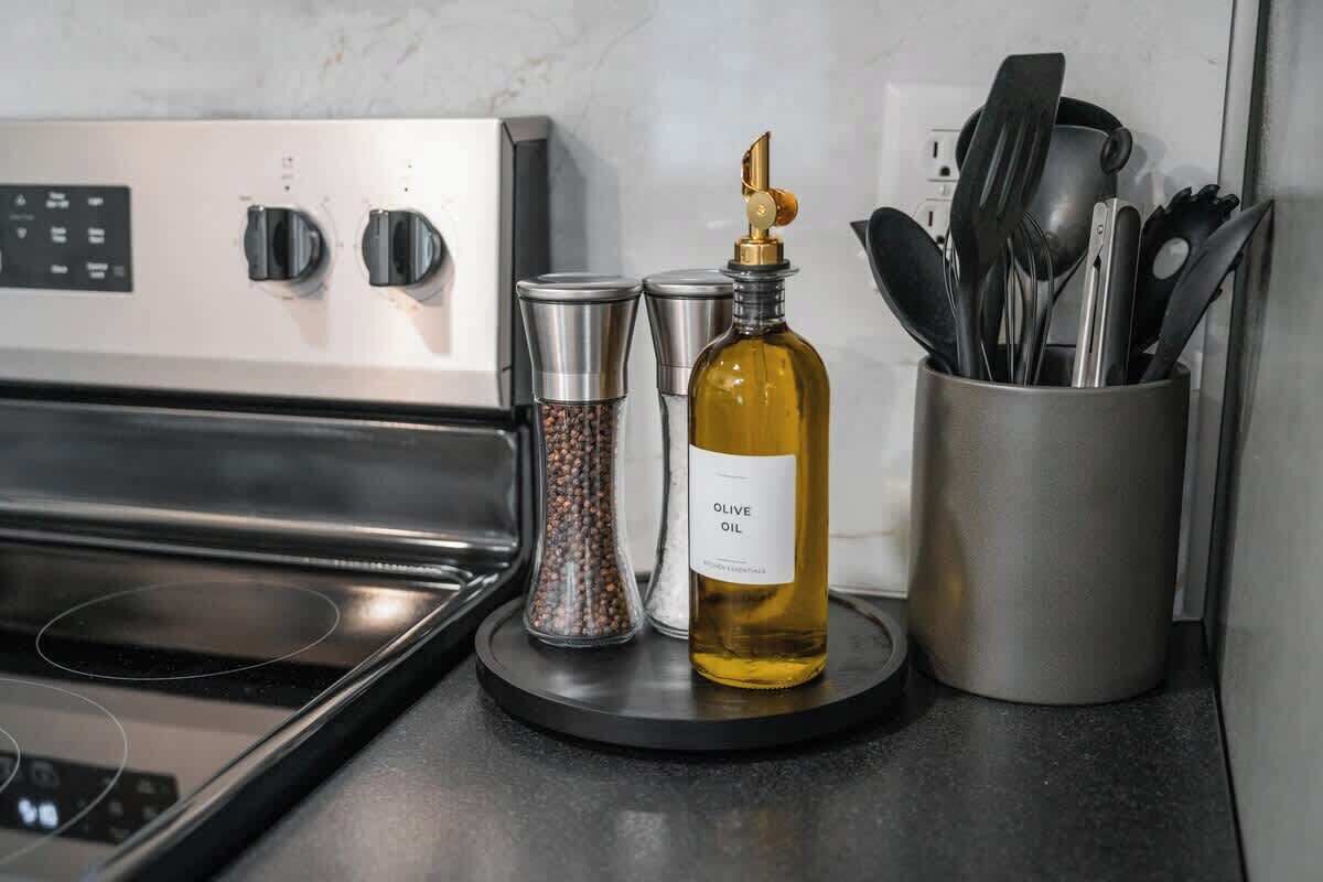 A kitchen counter with a stove, a bottle of olive oil, a pepper grinder, and a utensil holder.
