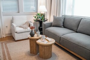 A living room with a grey sofa, a white armchair, two wooden side tables, a lamp, and a potted plant. - The Bluebird | Pet-Friendly 2BR Apt Near Hershey (Elizabethtown)