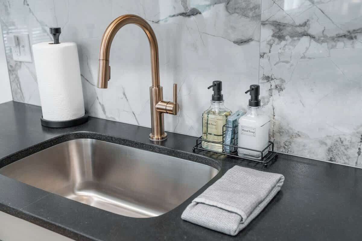 A bathroom sink with a modern faucet, a marble backsplash, and toiletries on the counter.