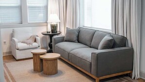 A modern living room with a grey sofa, a white armchair, and two round wooden side tables.