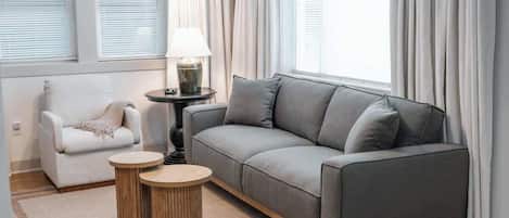 A modern living room with a grey sofa, a white armchair, and two round wooden side tables.