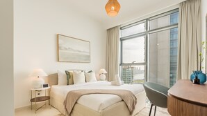 A modern bedroom with a large bed, bedside lamps, a desk, and a view of the city through large windows. - Prime Waterfront Location with Stunning Palm Jumeirah Views, Close to Dubai’s Top Attractions (Dubai)