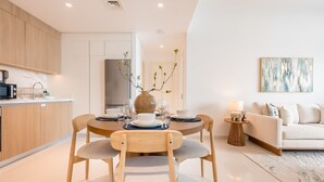 A modern kitchen with wooden cabinets, a dining table set for four, and a living area with a sofa and a lamp. - Prime Waterfront Location with Stunning Palm Jumeirah Views, Close to Dubai’s Top Attractions (Dubai)