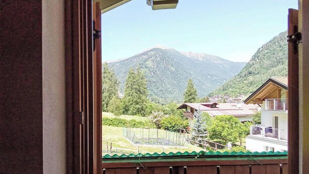 Vista de la montaña desde una ventana con balcón, un edificio de madera y un jardín cercado.