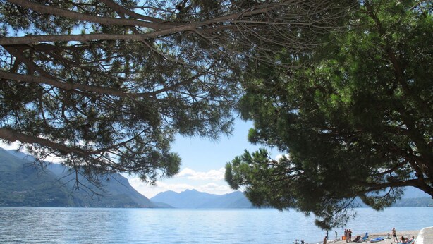 Vista para um lago com praia, montanhas ao fundo e pessoas nadando e relaxando.