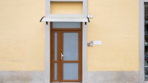 Un bâtiment à la façade jaune, une porte en bois avec un panneau de verre et un petit auvent au-dessus de la porte.