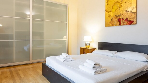 Une chambre d’hôtel avec un lit, une table de chevet avec une lampe et une grande fenêtre avec du verre dépoli.