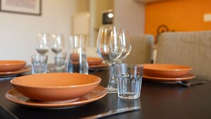 Une table à manger dressée avec des assiettes orange, des verres transparents et quelques verres à vin.