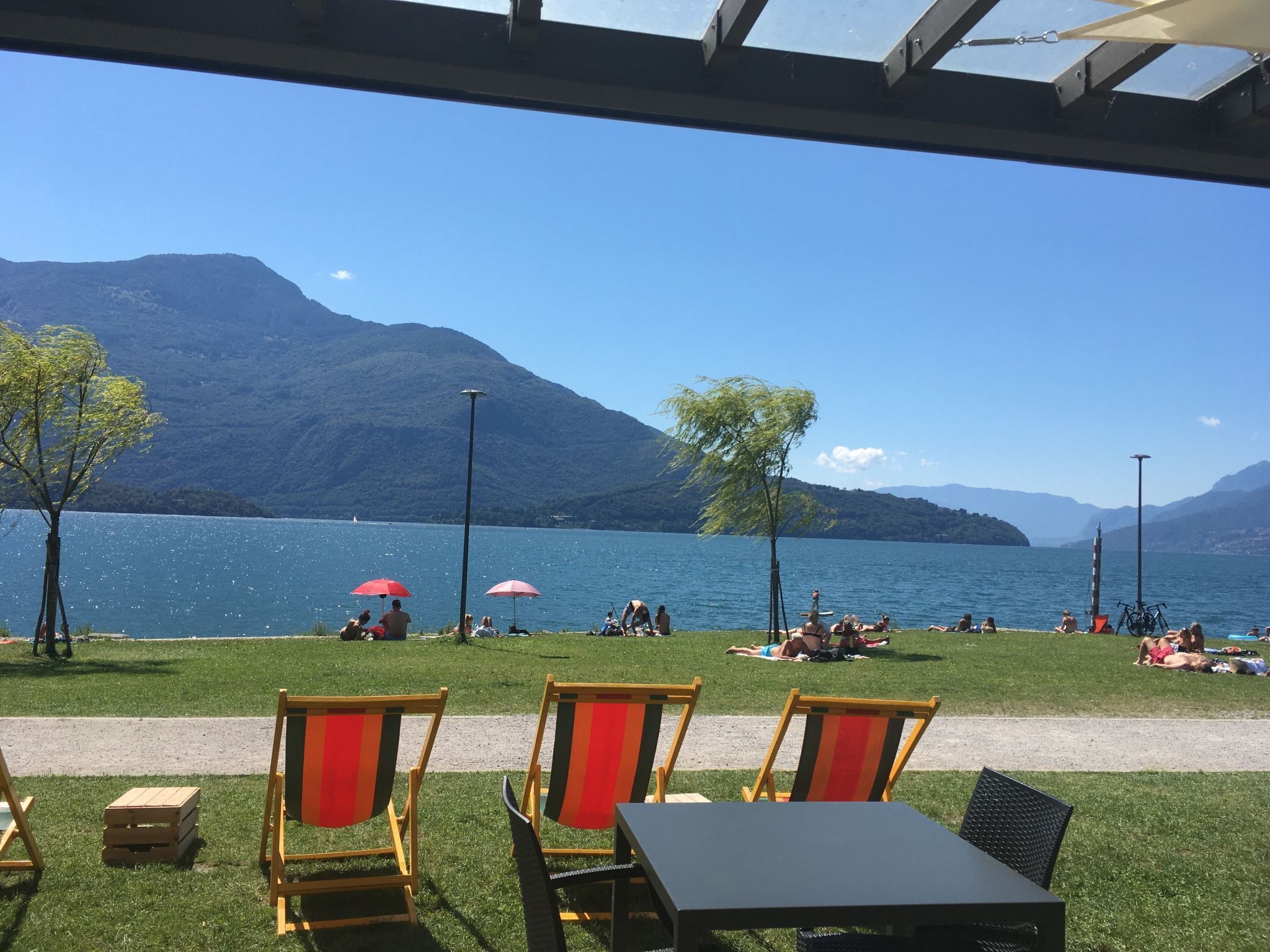An outdoor seating area with chairs and tables, overlooking a lake with mountains in the background.