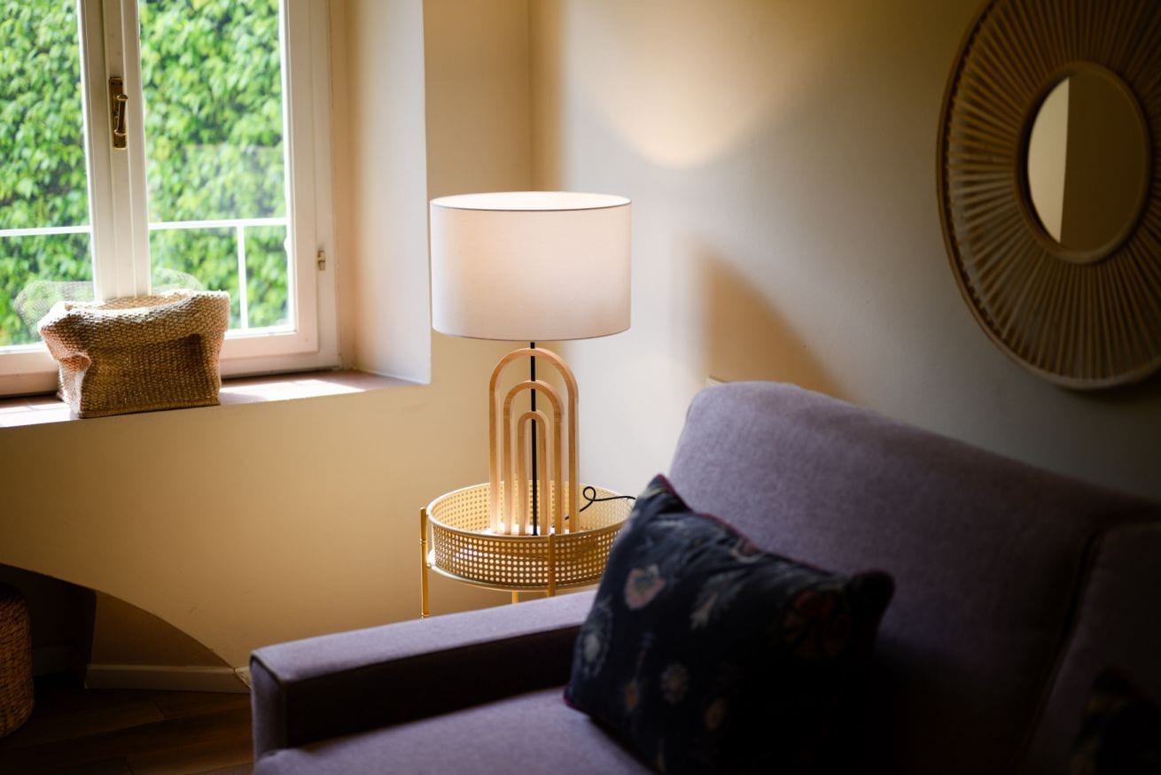 A room with a window, a lamp, a cushion, and a wall decoration.