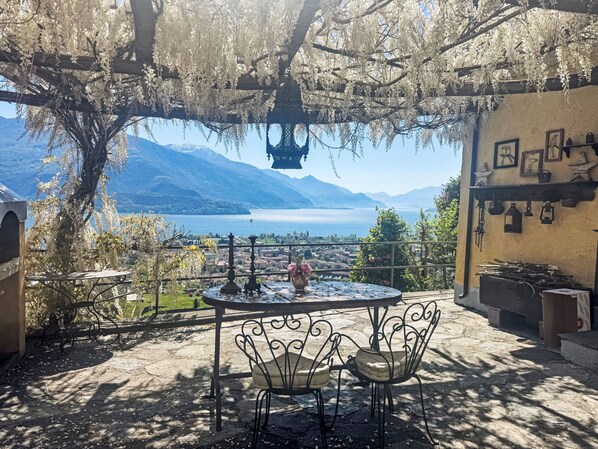 Une terrasse avec une table et des chaises, une vue sur un lac, des montagnes et un bâtiment orné de tableaux encadrés.