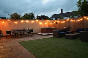 A patio with a wooden fence, string lights, a barbecue grill, and outdoor seating. - The Nook | Cotswolds Home | HOT TUB | Sleeps 9 (Eastington)