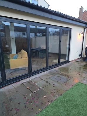A modern house with a large sliding glass door leading to a patio area. - The Nook | Cotswolds Home | HOT TUB | Sleeps 9 (Eastington)