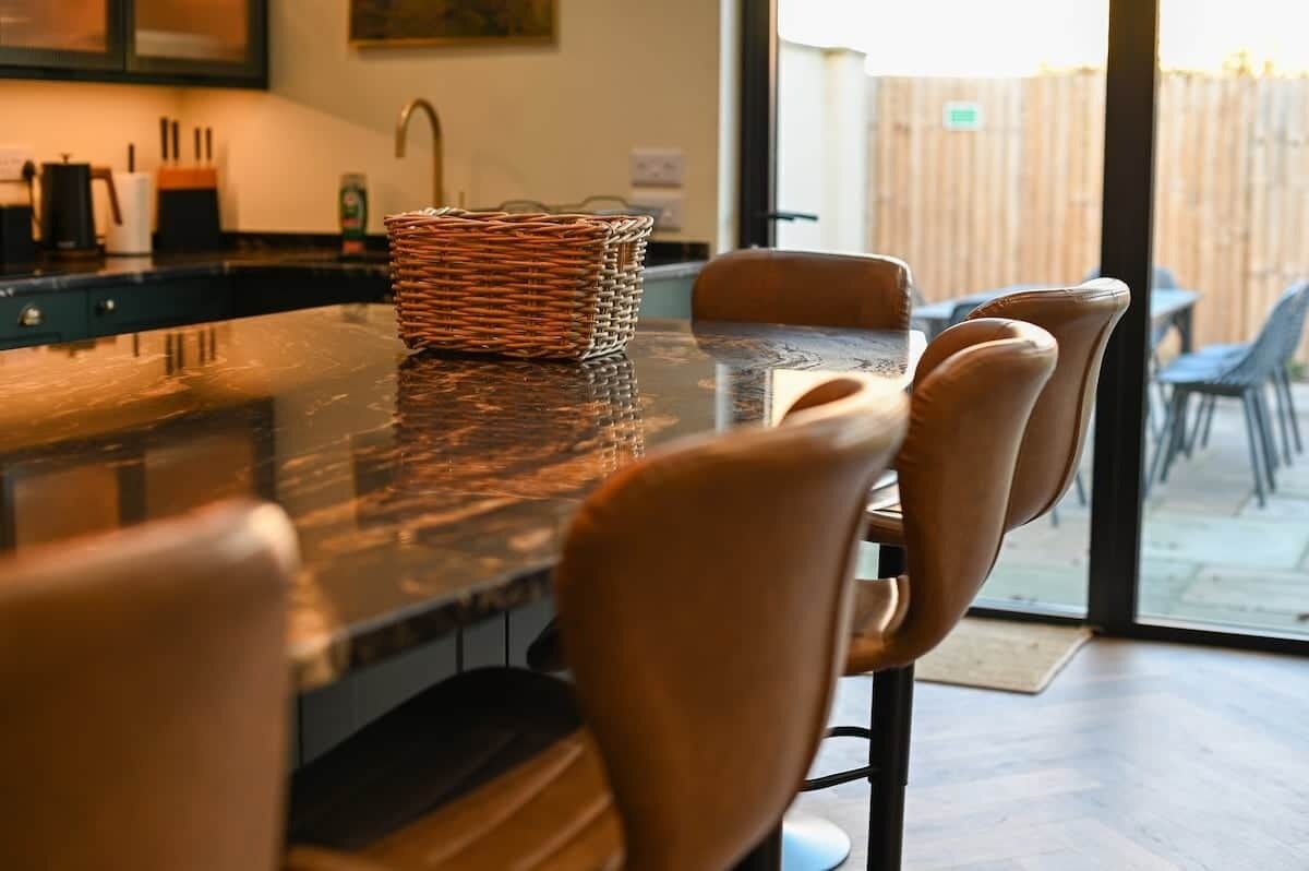 Un espace repas comprenant une longue table, des chaises, un panier en osier et une vue sur l’extérieur.