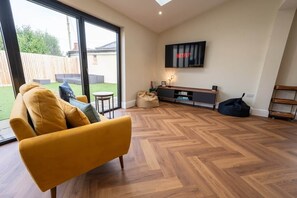 Una sala de estar moderna con un sofá amarillo, un televisor montado en la pared y un suelo de madera en patrón de espiga.