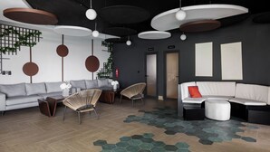 Ein modernes Wohnzimmer mit einem grauen Sofa, zwei Korbstühlen, einem weißen Sofa mit rotem Kissen und einem Teppich mit sechseckigem Muster.