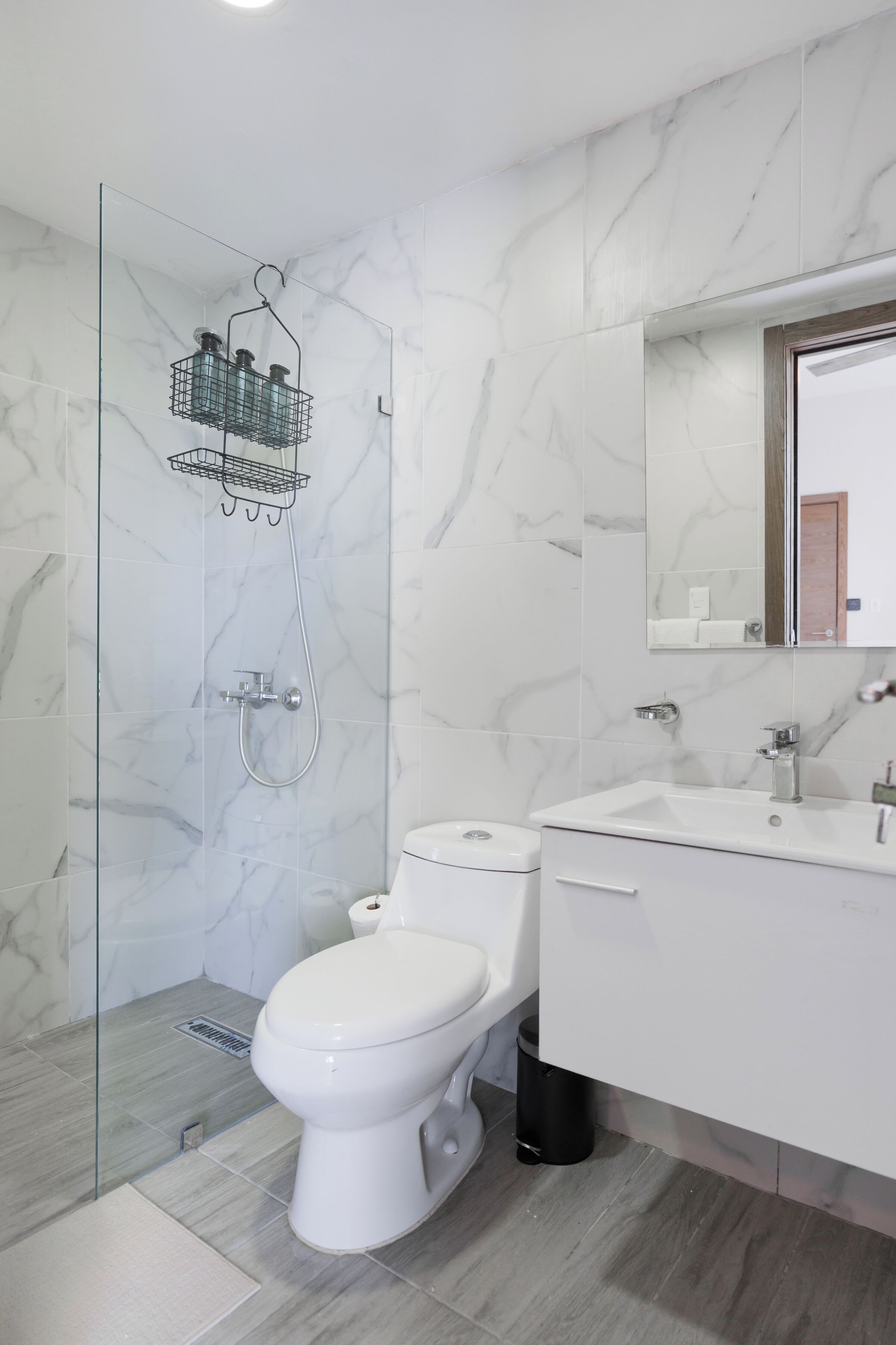 Et moderne badeværelse med et glasafskærmet brusebad, et hvidt toilet og et vaskeskab med spejl.