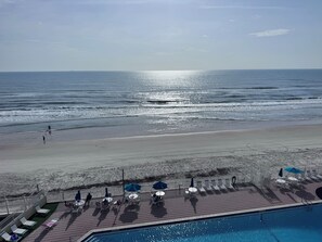 A poolside area with lounge chairs and umbrellas, a pool, and a view of the beach and ocean. - Perfect Weekend Getaway-Balcony (Daytona Beach)